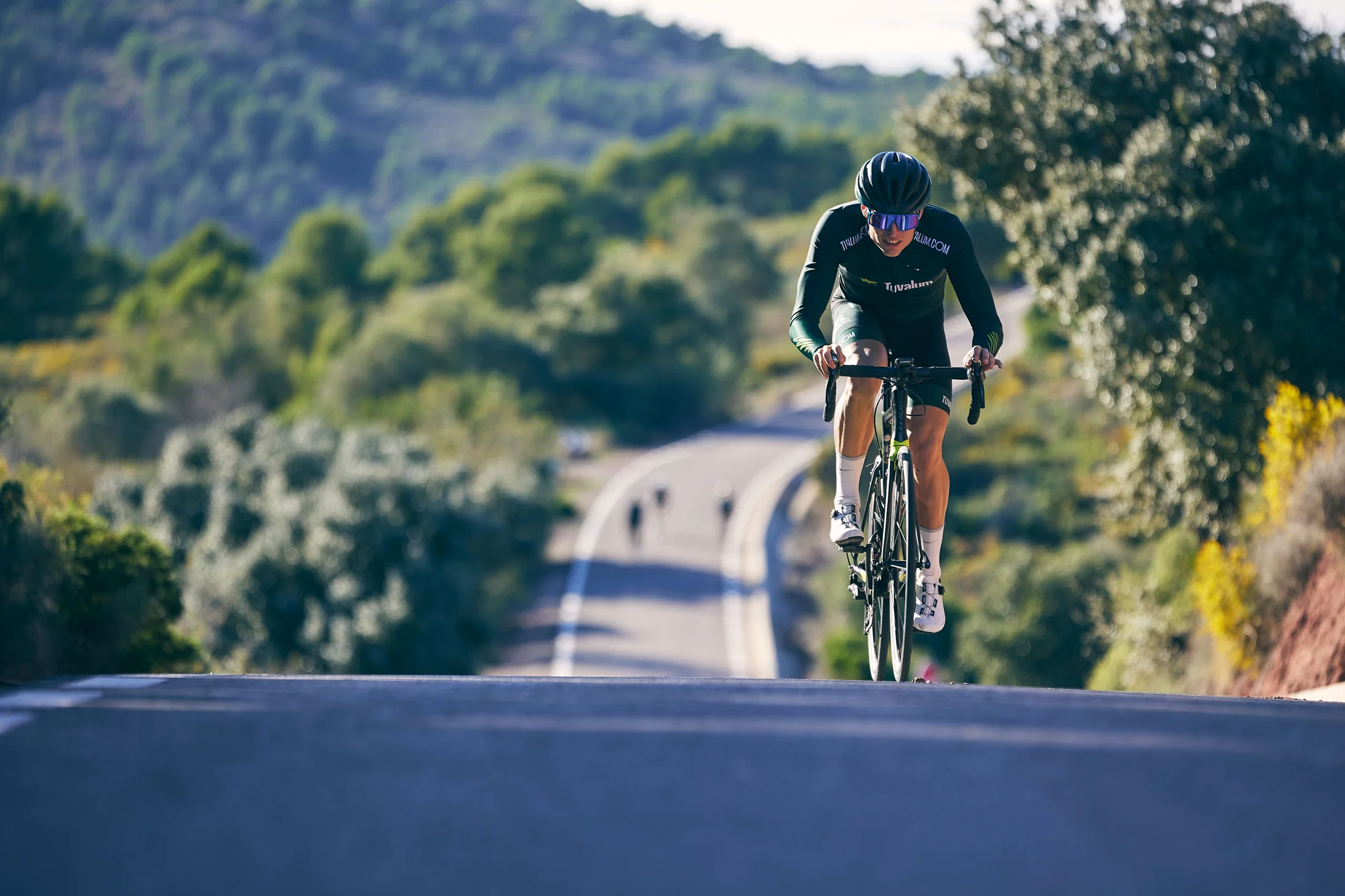 A helmeted road cyclist climbing a quiet road through green hills